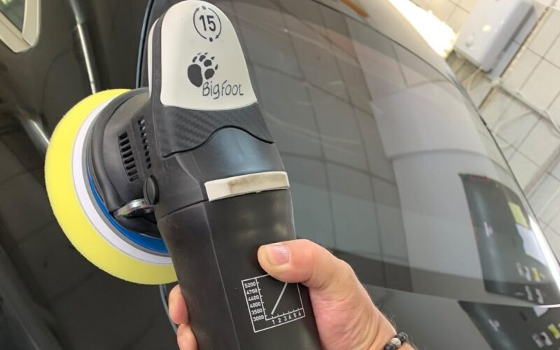 Exzenterpoliermaschine mit gelbem Polierpad bei der Lackaufbereitung an einem dunklen Fahrzeug